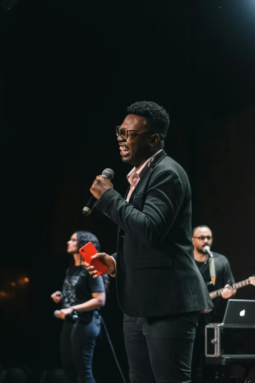 a man standing on top of a stage holding a microphone, an album cover, pexels, godwin akpan, in church, singing, square