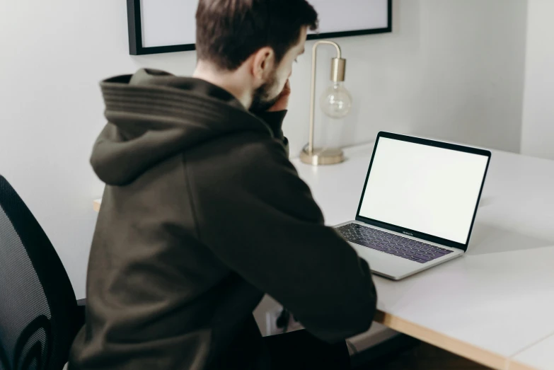 a man sitting at a desk using a laptop computer, trending on pexels, wearing a grey hooded sweatshirt, avatar image, casey cooke, sitting in an empty white room