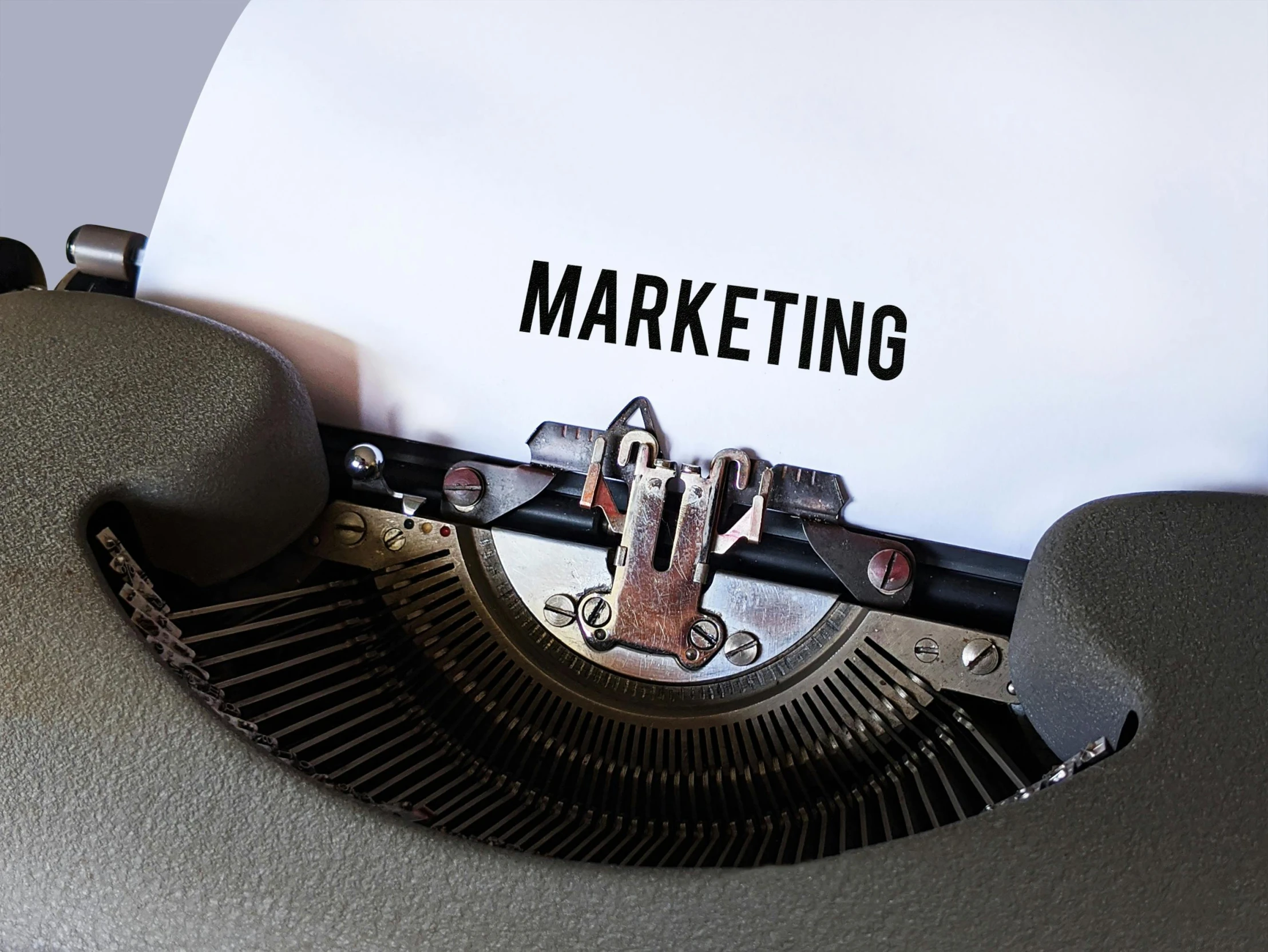 a typewriter with a paper that says marketing, on grey background, tin foiling, thumbnail, digital image