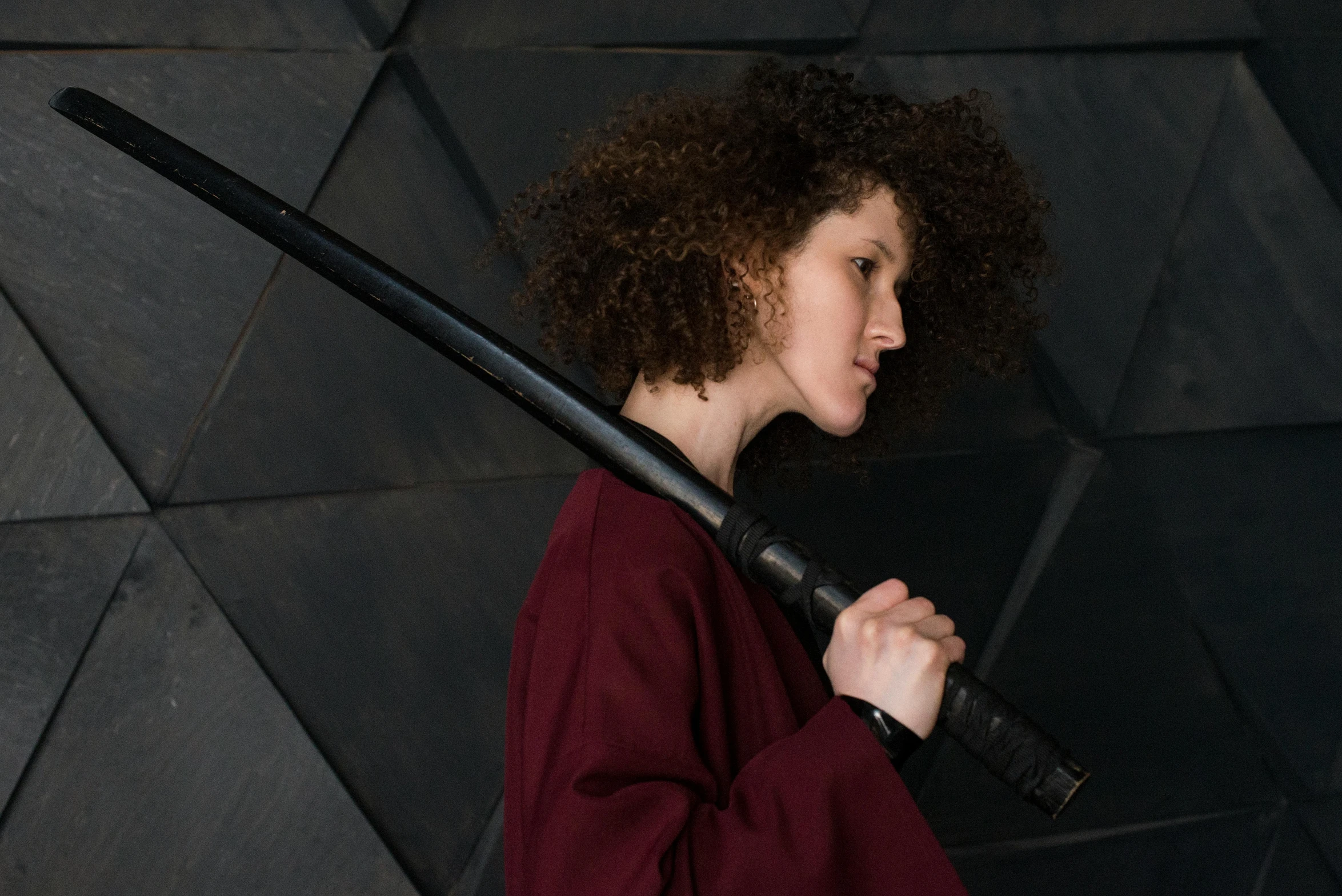 a woman holding a baseball bat in front of a wall, inspired by Kanō Hōgai, pexels contest winner, renaissance, brown jedi robe, afro futuristic, activity with fight on swords, portrait of arya stark