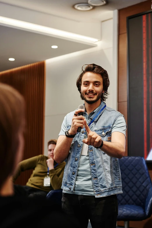 a man standing in front of a group of people, a picture, happening, holding a microphone, student, avatar image, eng kilian