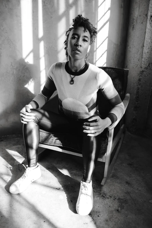 a black and white photo of a man sitting in a chair, by Jessie Alexandra Dick, trending on pexels, afrofuturism, short platinum hair tomboy, with prison clothing, with a ponytail, high view