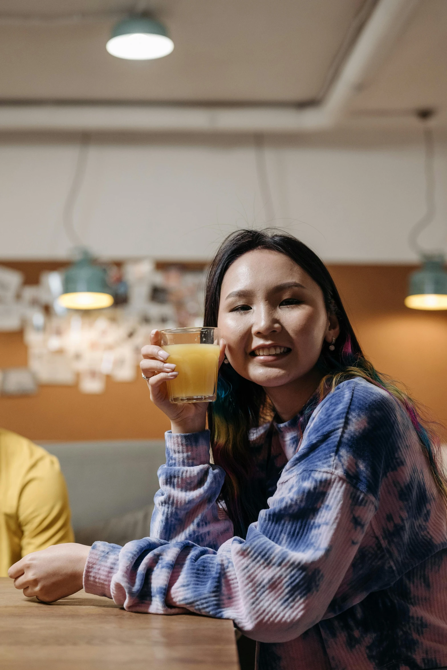 a woman sitting at a table with a cup of coffee, wearing a yellow hoodie, ruan jia and brom, juice, inuit