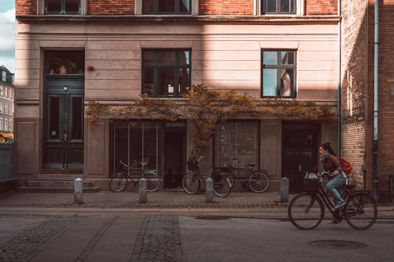 a person riding a bike in front of a building, by Jesper Knudsen, coffee shop, fall season, summer afternoon, old building