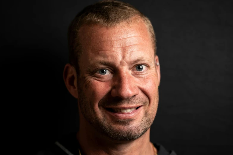 a man smiling in front of a black background, a picture, by Salomon van Abbé, karch kiraly, 40 years old women, profile image, simon stälenhag