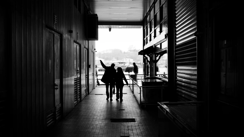 a couple of people walking down a hallway, a black and white photo, pexels contest winner, standing on a ship deck, exiting store, silhouette!!!, central station in sydney
