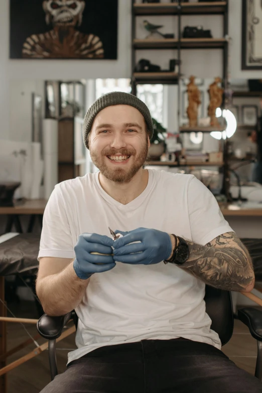 a man sitting in a chair with a tattoo on his arm, a tattoo, inspired by Seb McKinnon, happily smiling at the camera, holding a magic needle, partially cupping her hands, dominik mayer