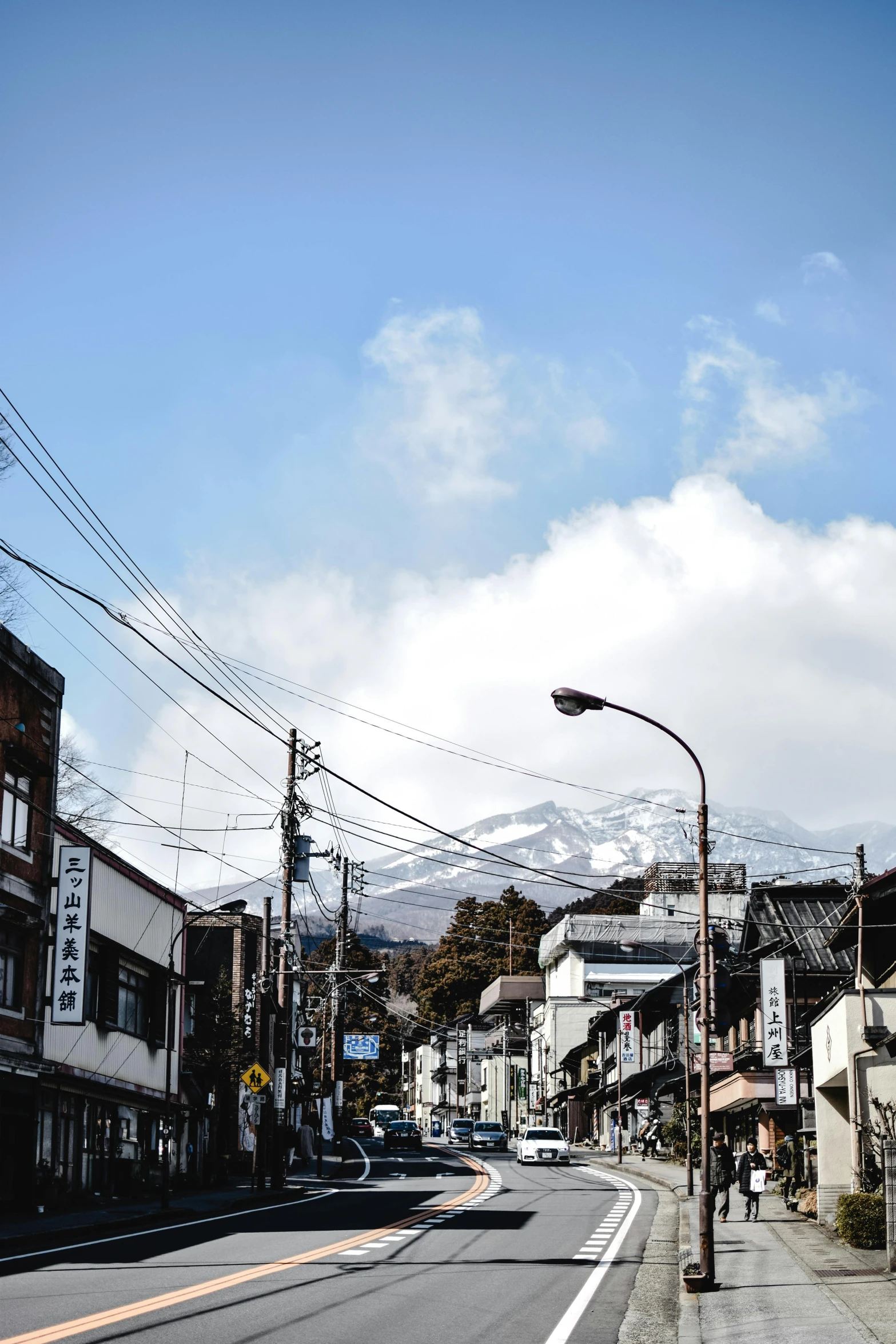 a city street with a mountain in the background, inspired by Okamoto Tarō, unsplash, mingei, white steam on the side, wires hanging above street, with snow on its peak, square