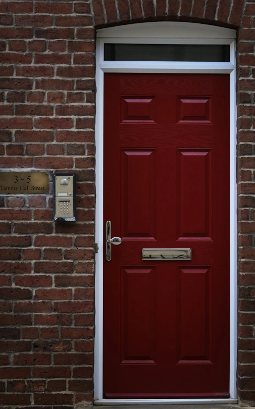 a red door in front of a brick building, a picture, by David Simpson, pexels, paul barson, an intruder, panoramic shot, brass