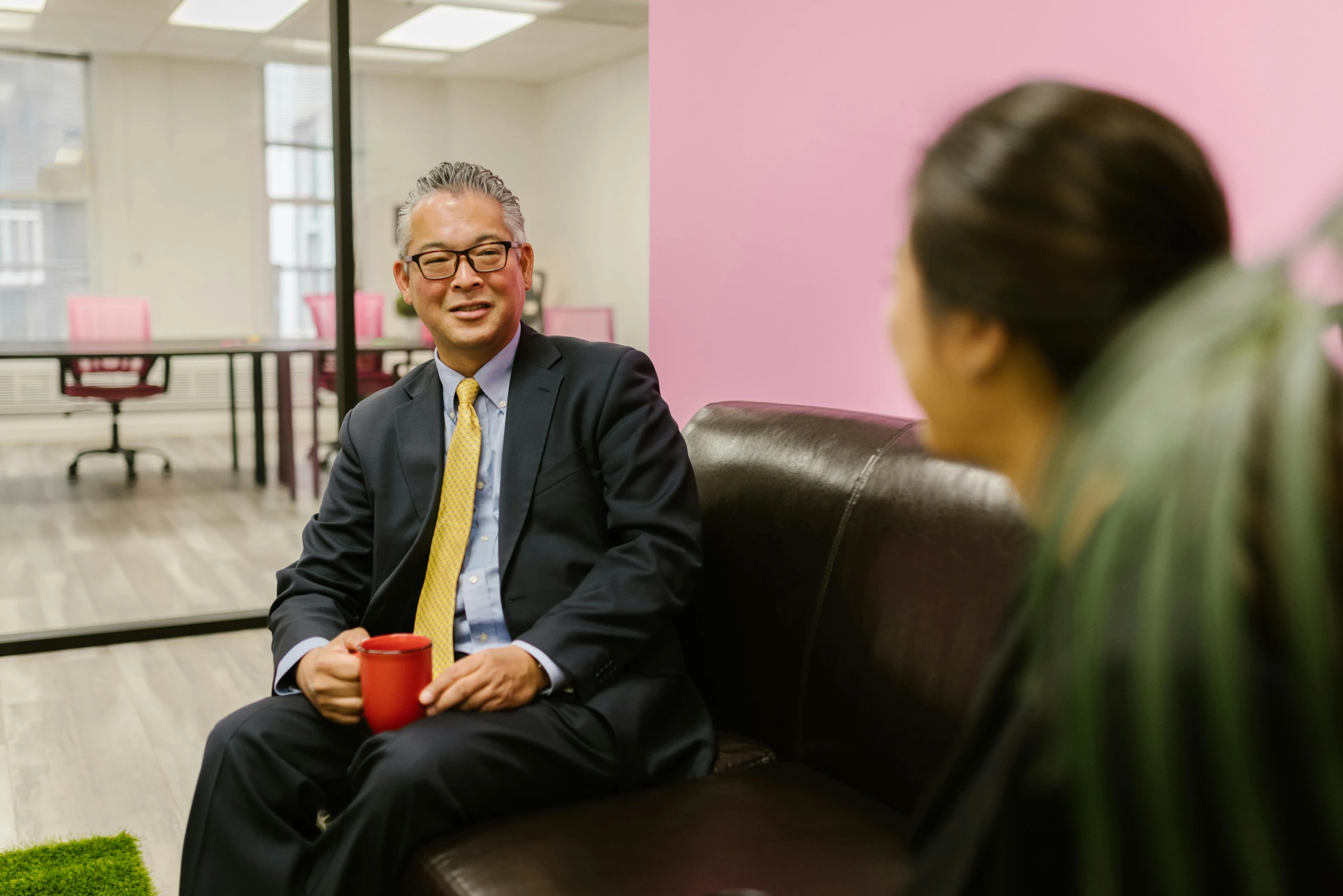 a man sitting on top of a couch next to a woman, unsplash, gutai group, wearing a light - pink suit, in office, paul lung, friendly face