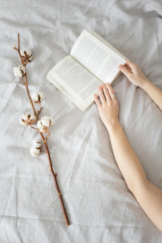 a person laying on a bed reading a book, by Grace Polit, pexels contest winner, holding flowers, cotton, but minimalist, wearing a linen shirt
