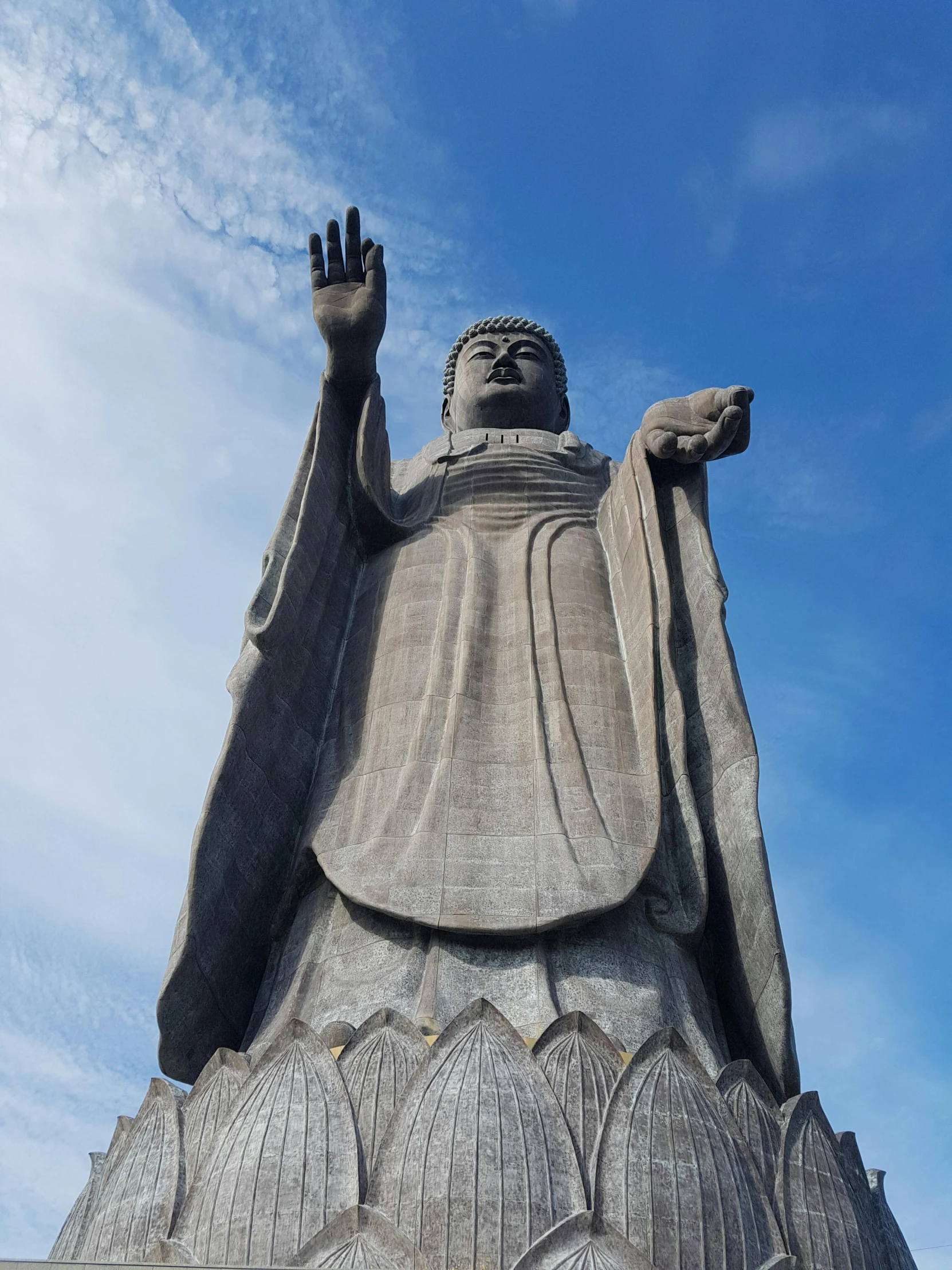 a large statue sitting on top of a lush green field, inspired by Kōshirō Onchi, unsplash, sōsaku hanga, wave a hand at the camera, 🚿🗝📝, wearing a grey robe, guanyin of the southern seas