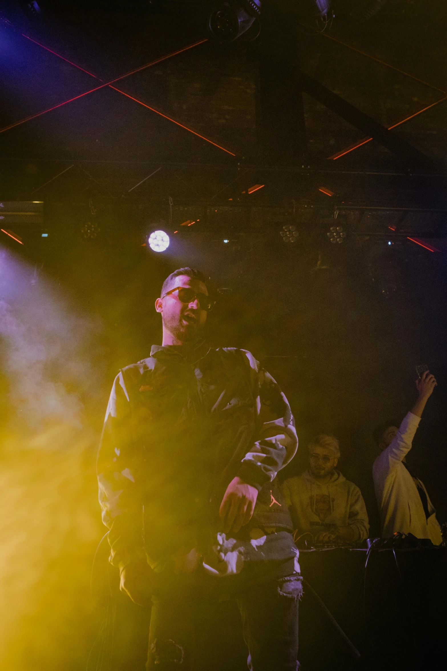 a man standing on top of a stage holding a microphone, by Robbie Trevino, pexels, holography, “house music rave with dancers, wearing camo, doug walker, trenches