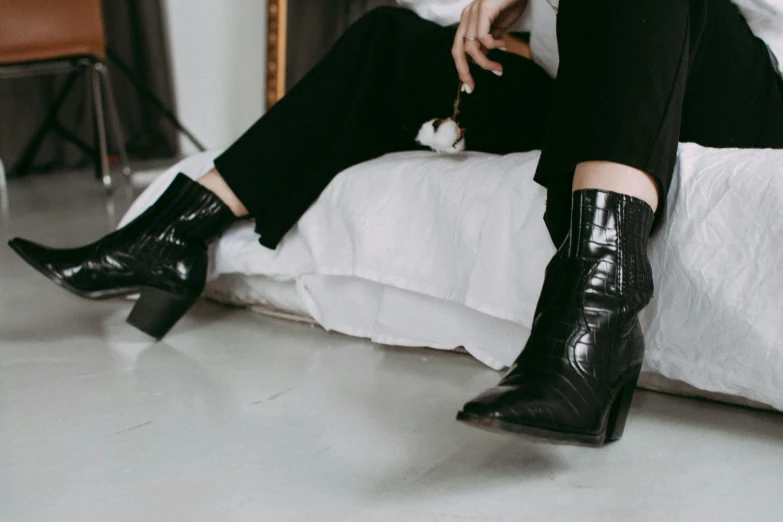 a woman sitting on a bed wearing black boots, trending on pexels, wearing fancy clothes, western clothing, patent style, on a white table
