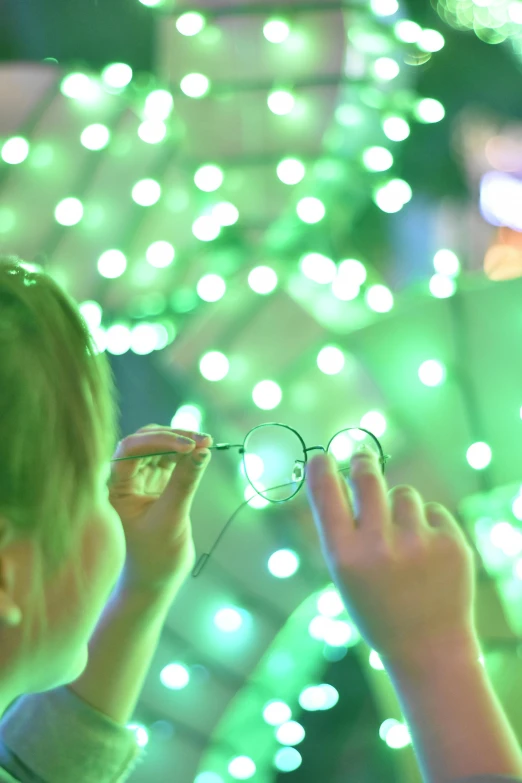 a couple of kids that are standing in front of a christmas tree, inspired by Bruce Munro, pexels, interactive art, detail shot, circular glasses, light green, lit. 'the cube'