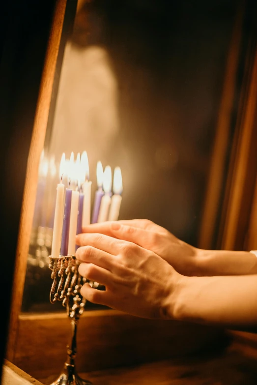 a person lighting a menorah in front of a mirror, softly - lit