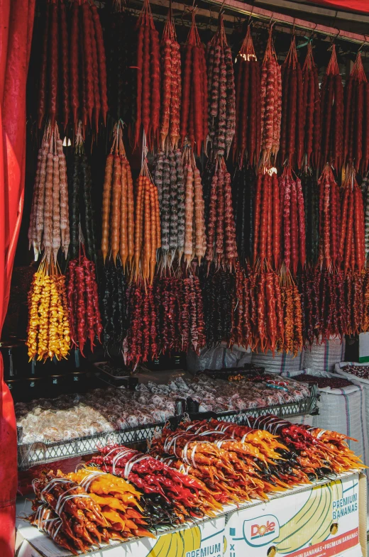 a man standing in front of a food stand, red intricate long braids, dark oranges reds and yellows, made of cactus spines, hanging beef carcasses