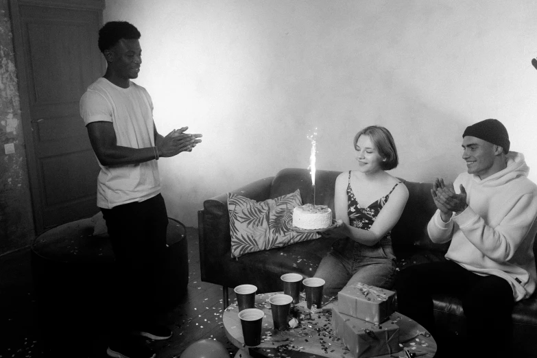 a group of people sitting around a table with a cake, a black and white photo, by Alice Mason, 2 1 savage, birthday cake, desaturated!!, mkbhd