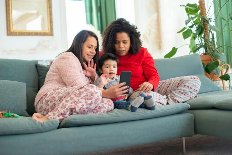 a couple of women sitting on top of a couch next to a baby, a picture, pexels, happening, checking her phone, english, screensaver, husband wife and son