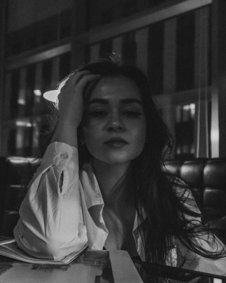 a black and white photo of a woman sitting at a table, inspired by Elsa Bleda, unsplash contest winner, realism, lucy hale, looking tired, in the night, hailee steinfeld