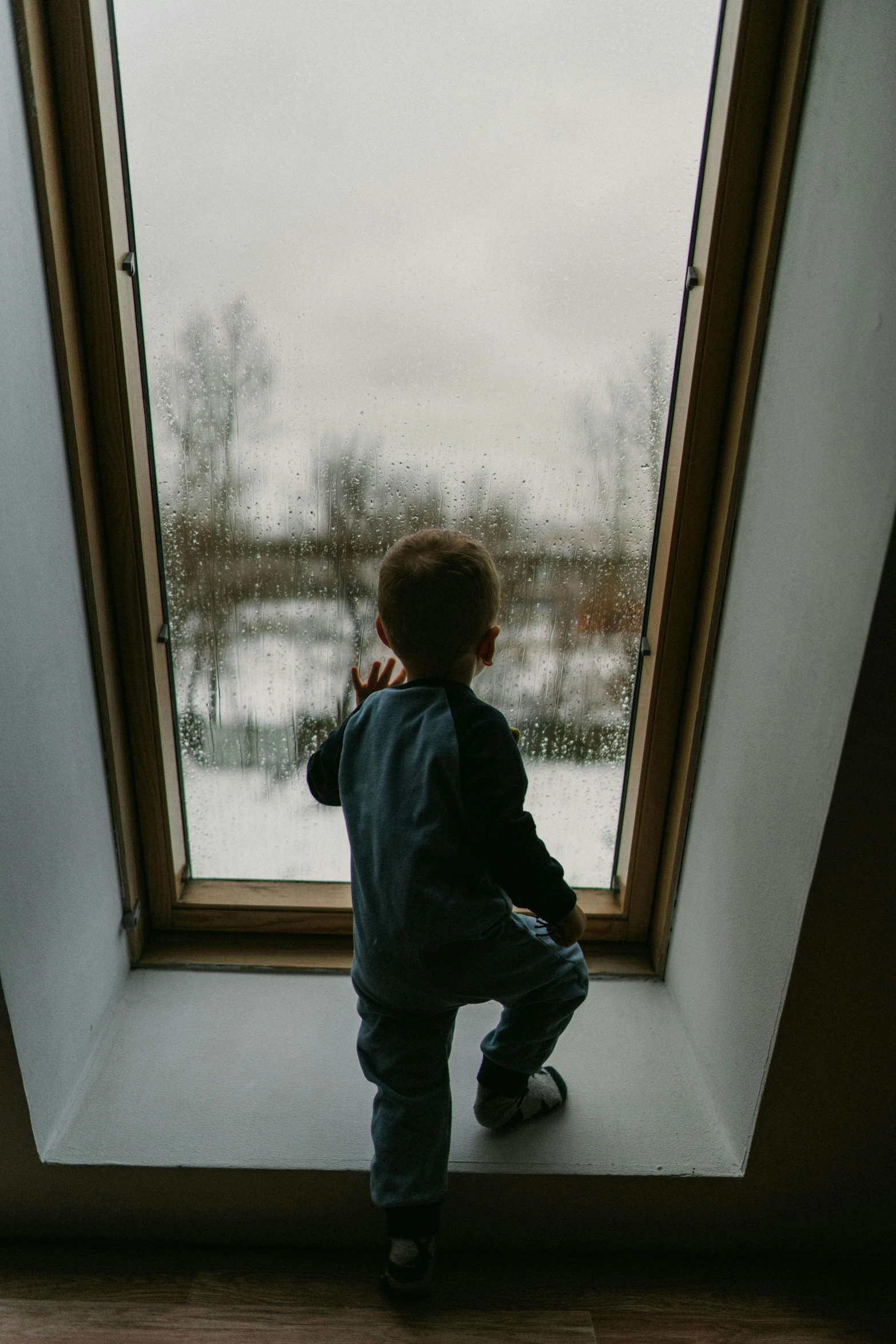 a little boy that is standing in front of a window, in the snow