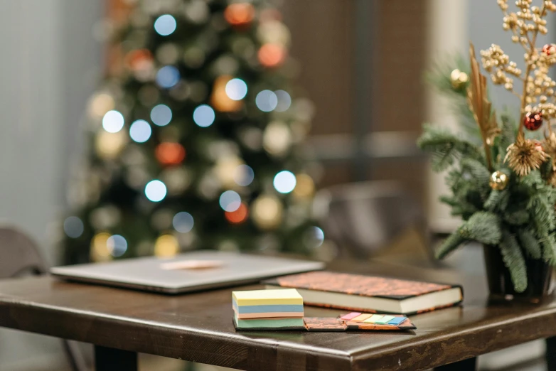 a wooden table topped with books next to a christmas tree, a portrait, pexels, happening, desk, coloured, where a large, gif