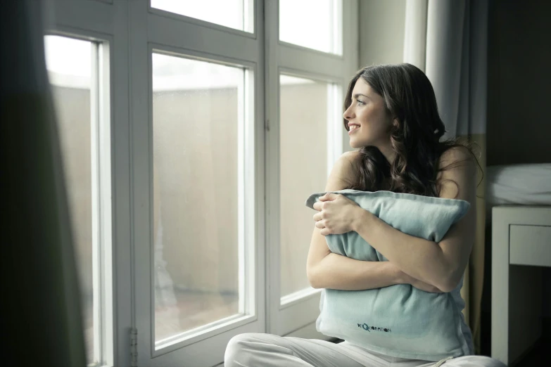 a woman sitting in front of a window holding a pillow, aquamarine windows, happy cozy feelings, gray, medium