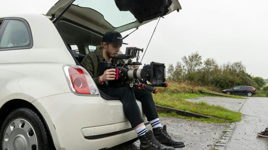 a man sitting in the trunk of a white car, unsplash, realism, arri alexa mini lf, red camera, production still, crane shot