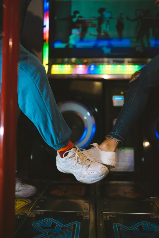 two people sitting in front of a video game machine, trending on unsplash, wearing white sneakers, dancefloor kismet, love story, jean and multicolor shoes