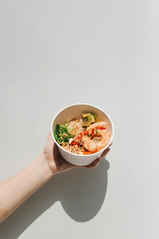 a person holding a bowl of food on a table, plain background, shrimp, from street level, bao pham