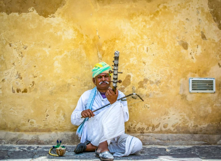 a man sitting on the ground with a pipe in his hand, pexels contest winner, dressed in a jodhpuri suit, songlines, square, yellow