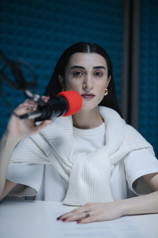 a woman sitting at a table in front of a microphone, inspired by Ion Andreescu, trending on reddit, nun fashion model, ana de la reguera portrait, lily frank, studio photo