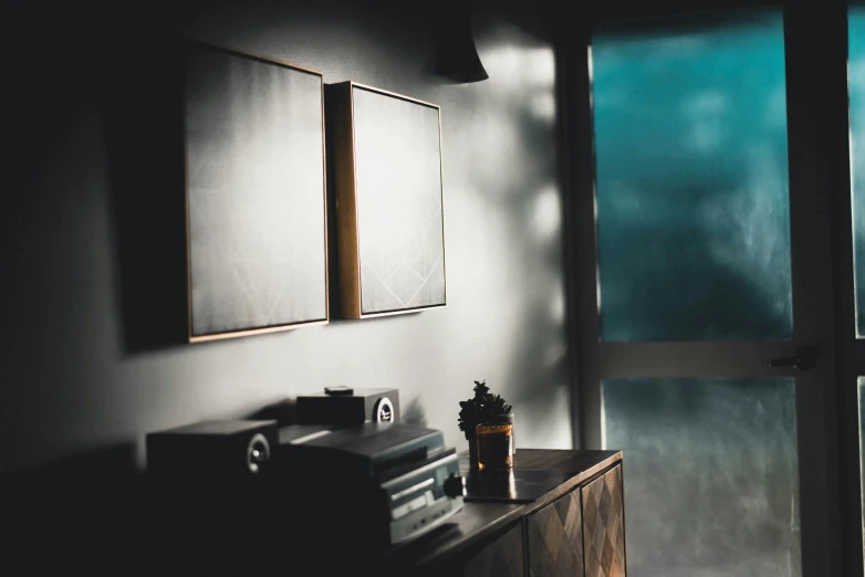 a room with two framed pictures on the wall, inspired by Elsa Bleda, unsplash contest winner, light and space, moody evening light, light reflecting off windows, underexposed grey, early morning light