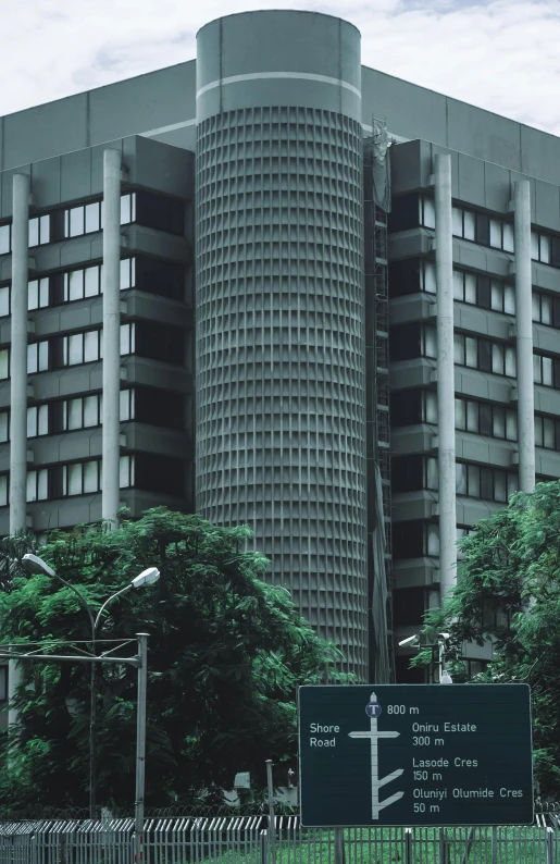 a tall building sitting on top of a lush green field, inspired by Cheng Jiasui, unsplash, brutalism, set in tokyo bank parking lot, desaturated!!, street view, late 1 9 6 0's