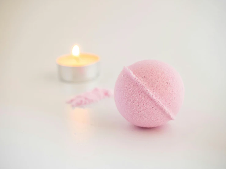 a pink bath ball sitting next to a lit candle, a picture, pexels, light blush, pastel', view, unedited