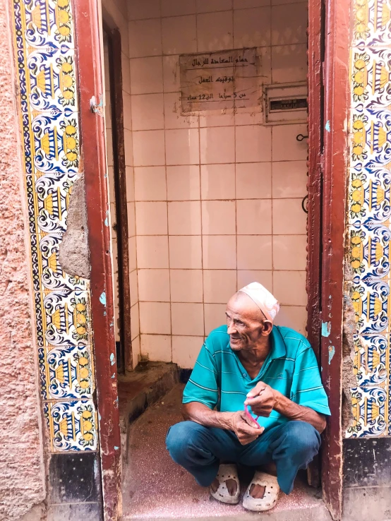 a man sitting in a doorway of a building, beautiful moorish tiles, 2019 trending photo, toilet, older male