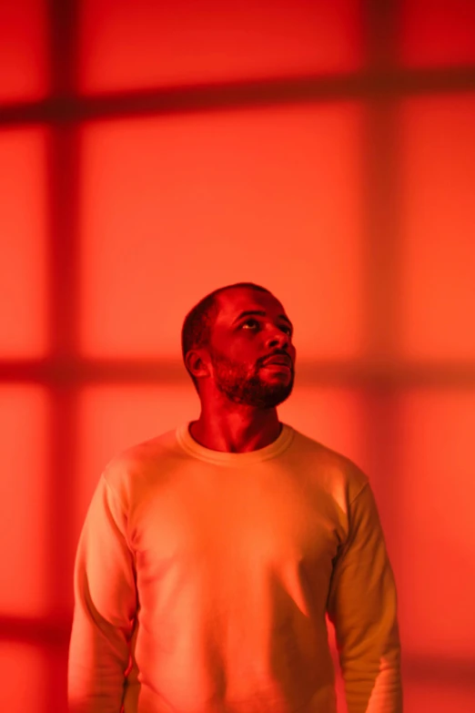 a man standing in front of a red wall, an album cover, inspired by Richard Wright, orange and red lighting, tyler, ap news photo, looking off to the side