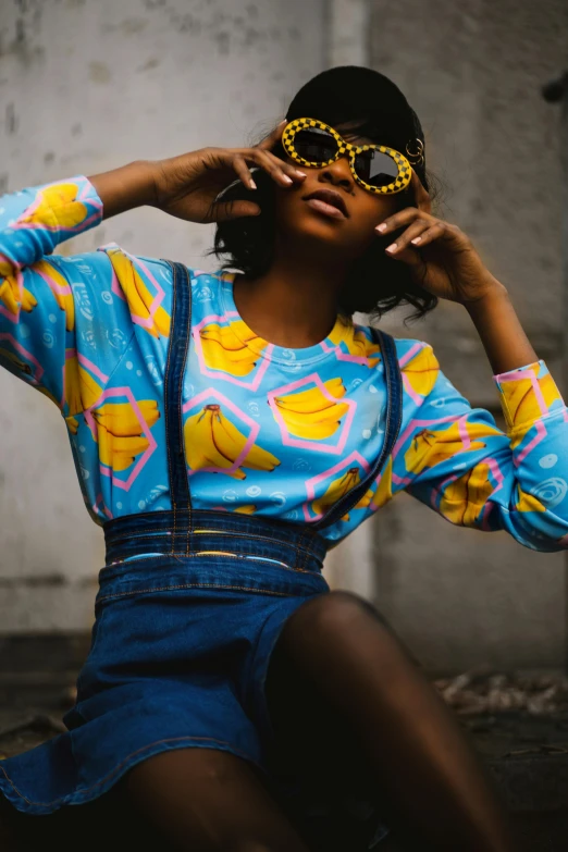 a woman sitting on the ground posing for a picture, inspired by Lubin Baugin, trending on pexels, afrofuturism, in blue and yellow clothes, vintage shirt, designer sunglasses, marge simpson