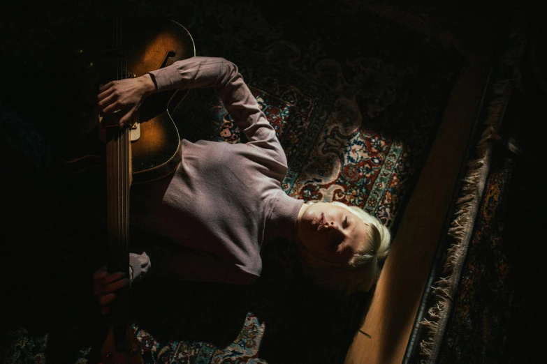 a person laying on the floor with a guitar, by Carey Morris, a blond, dramatic lighting from above, rhys lee, looking down on the camera