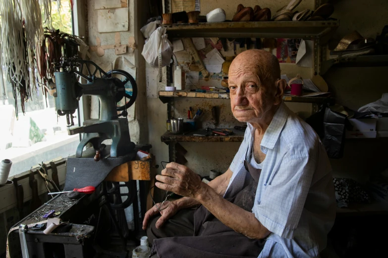 an old man sitting in front of a sewing machine, hila klein, photo taken in 2018, a tall, israel