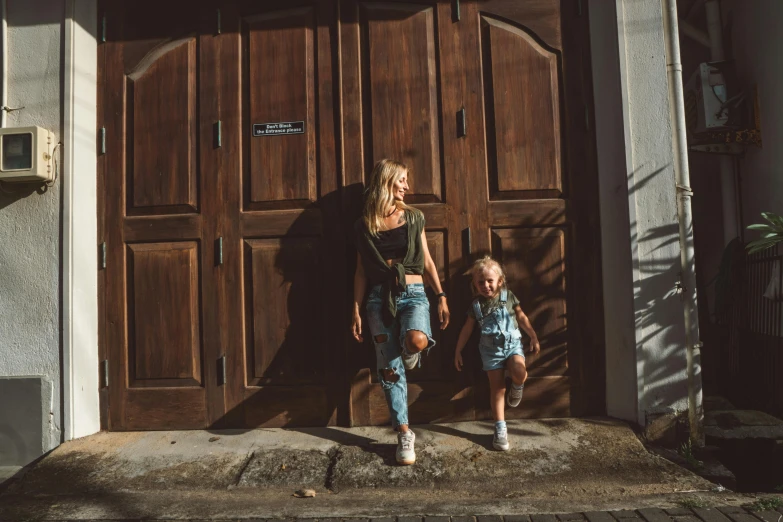 a woman and a child standing in front of a wooden door, by Emma Andijewska, pexels contest winner, baggy jeans, shady alleys, blonde, 15081959 21121991 01012000 4k