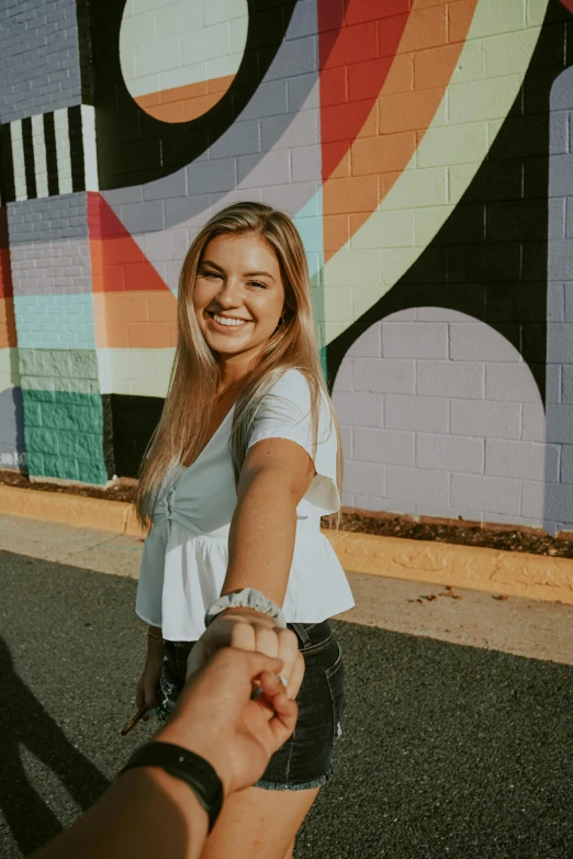 a woman holding a man's hand in front of a colorful wall, a black and white photo, trending on pexels, smiling girl, sydney hanson, 144x144 canvas, young blonde woman