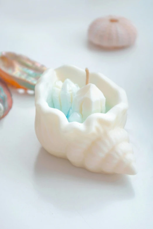 a white candle sitting on top of a white table, wearing seashell attire, colourful 3 d crystals, white and pale blue toned, open synthetic maw