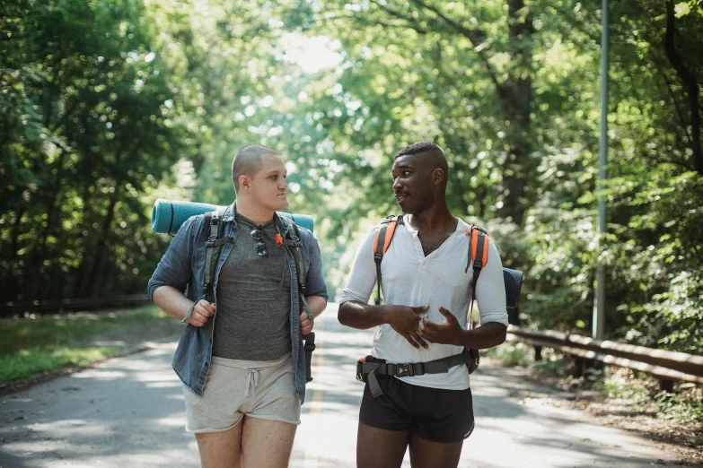 a couple of men standing next to each other on a road, by Emma Andijewska, pexels, happening, white shorts and hiking boots, non-binary, black man, in a park