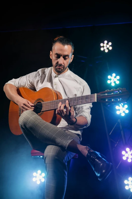 a man sitting on a stool playing a guitar, an album cover, inspired by Cándido López, pexels contest winner, antipodeans, square, performing on stage, headshot, artem