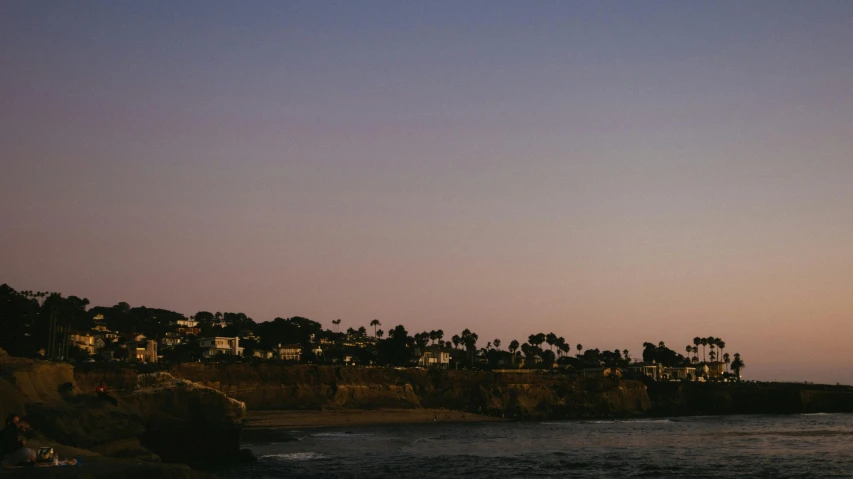 a person flying a kite on top of a beach, by Carey Morris, pexels, cliff side at dusk, neighborhood, oceanside, distant - mid - shot