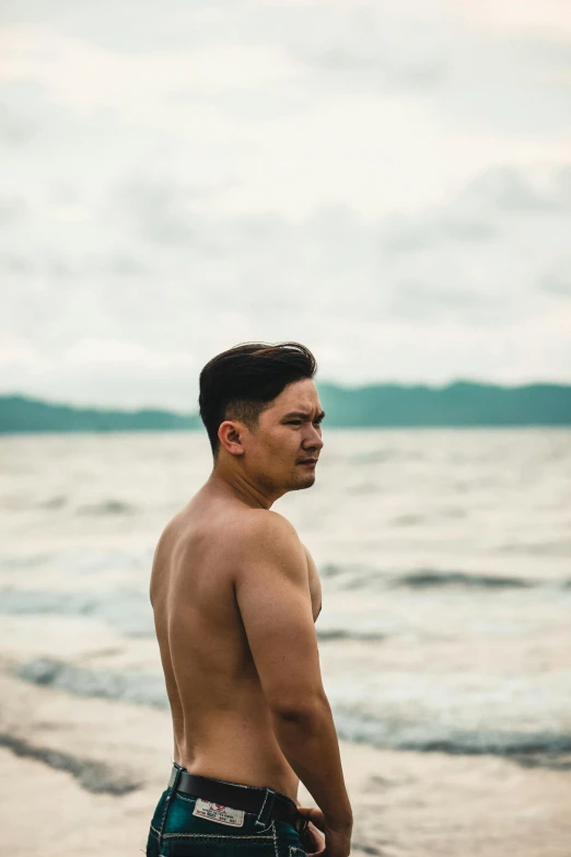 a man standing on a beach next to the ocean, an album cover, inspired by Byron Galvez, unsplash, sumatraism, handsome man, philippines, bare chest, leaked photo