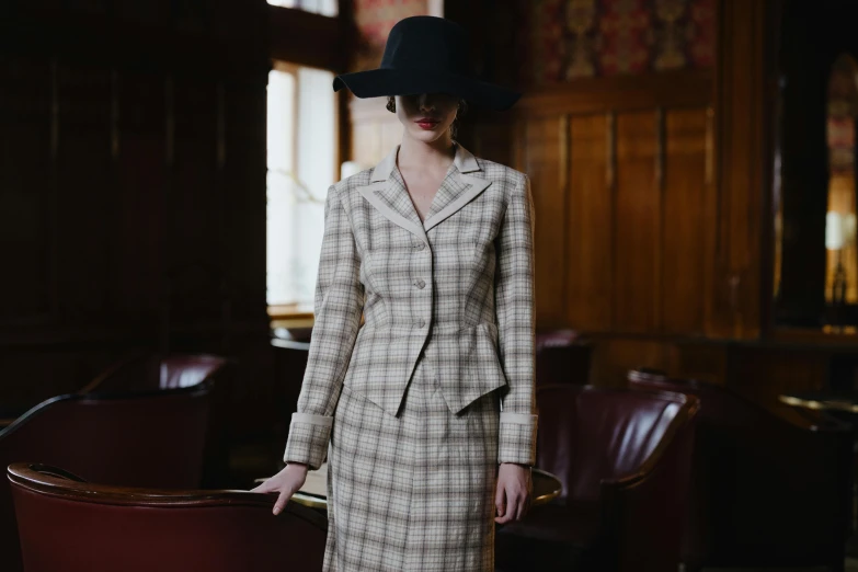 a woman in a suit and hat standing in a room, inspired by Pruett Carter, unsplash, renaissance, plaid skirt, square, beige, brown