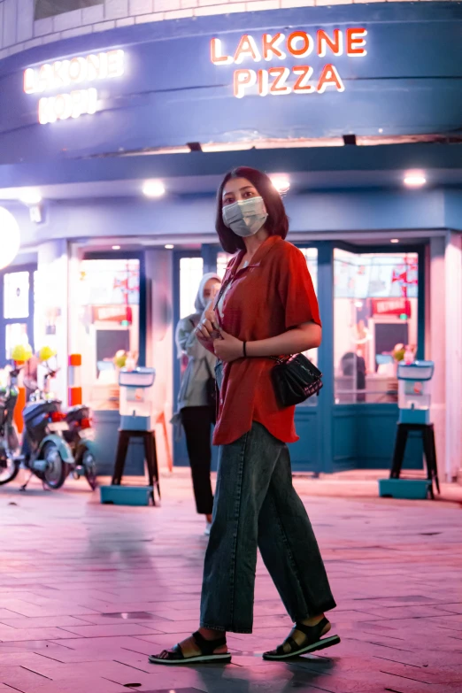 a woman wearing a face mask walking down a street, a picture, trending on pexels, malaysian, night life, square, shot on sony a 7