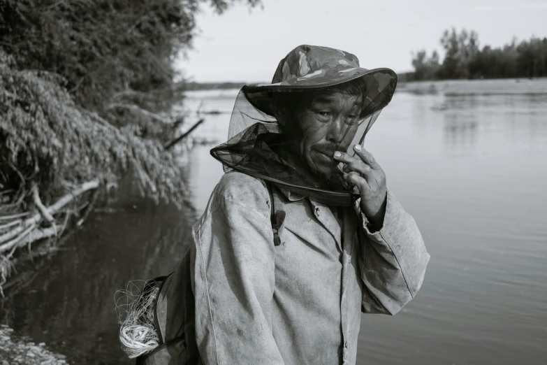 a man standing next to a body of water, inspired by Larry Fink, process art, chewing tobacco, fantasy beekeeper, vietnamese woman, still from nature documentary